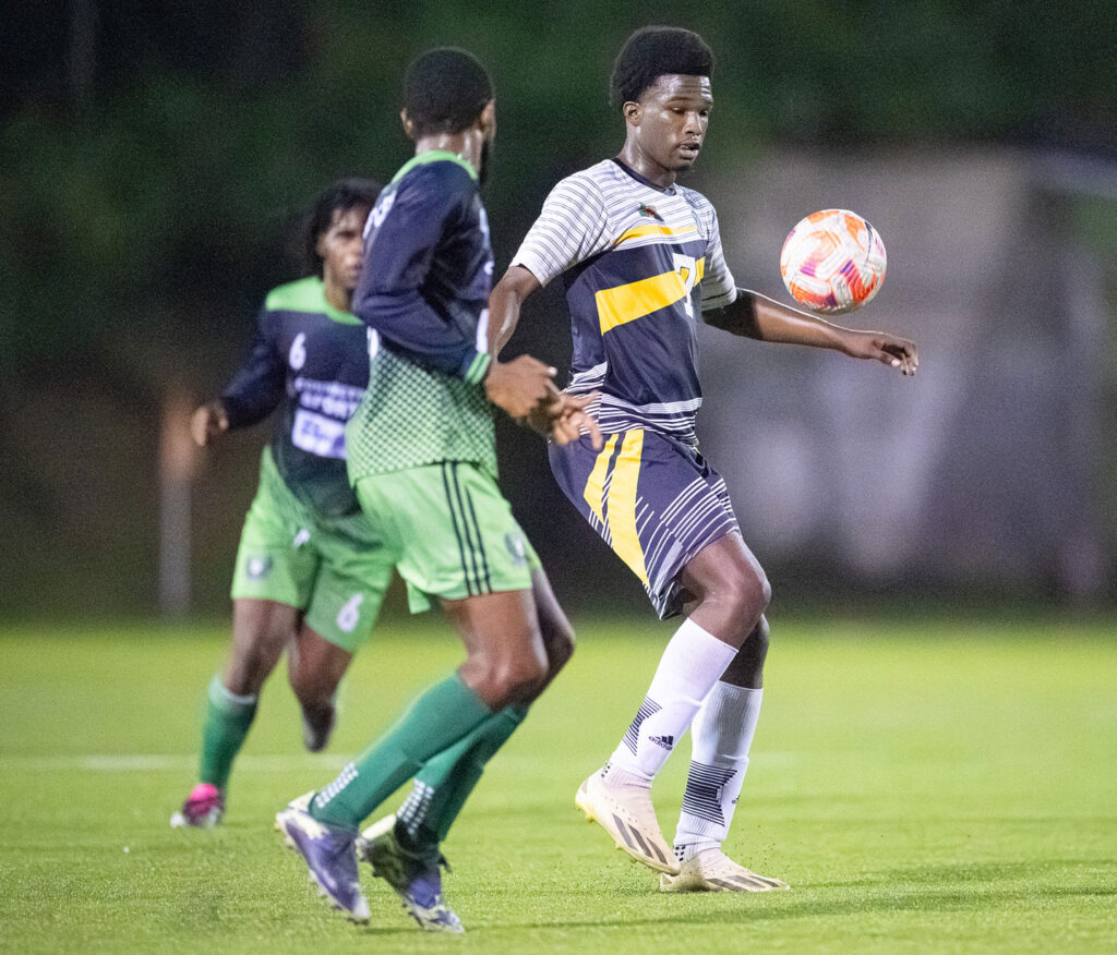 Middleham United FC player Josimar Gustave controlling a ball while surrounded by two East Central FC players